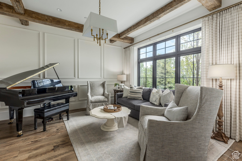 Living area with a decorative wall, beam ceiling, wood finished floors, and a chandelier