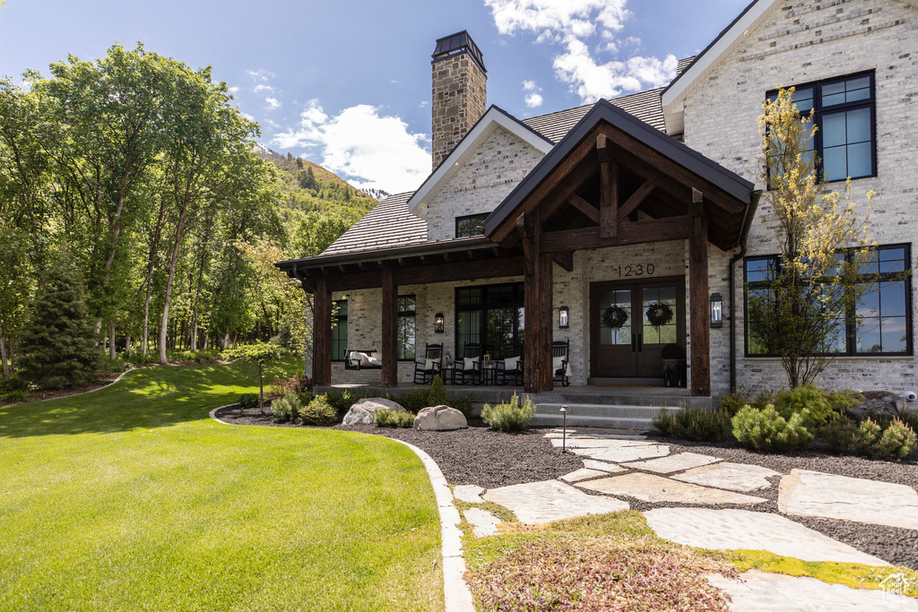 Doorway to property featuring a lawn, a chimney, brick siding, a porch, and french doors