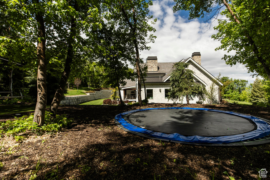 Rear view of property with a trampoline, a chimney, and a yard