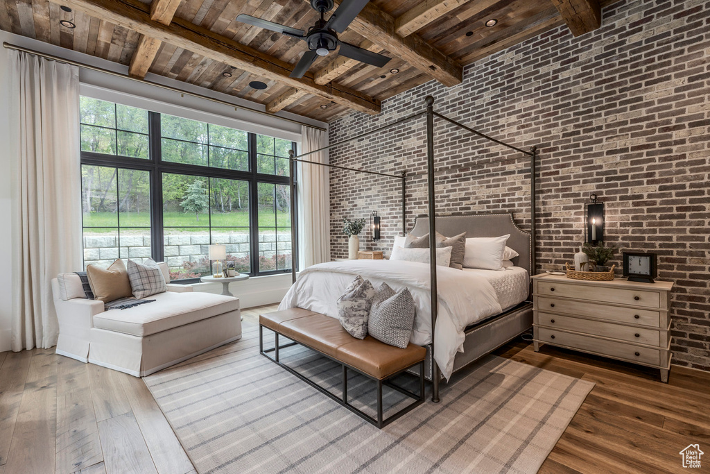 Bedroom with brick wall, wooden ceiling with exposed beams, hardwood / wood-style flooring, a towering ceiling, and multiple windows