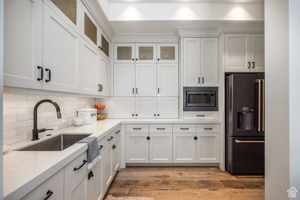 Kitchen with black fridge with ice dispenser, stainless steel microwave, a sink, light stone counters, and white cabinets