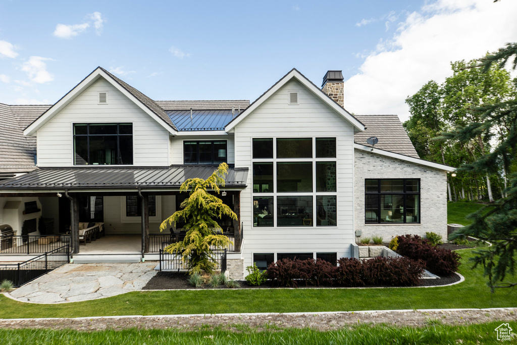 Back of property with a standing seam roof, metal roof, a lawn, and a chimney