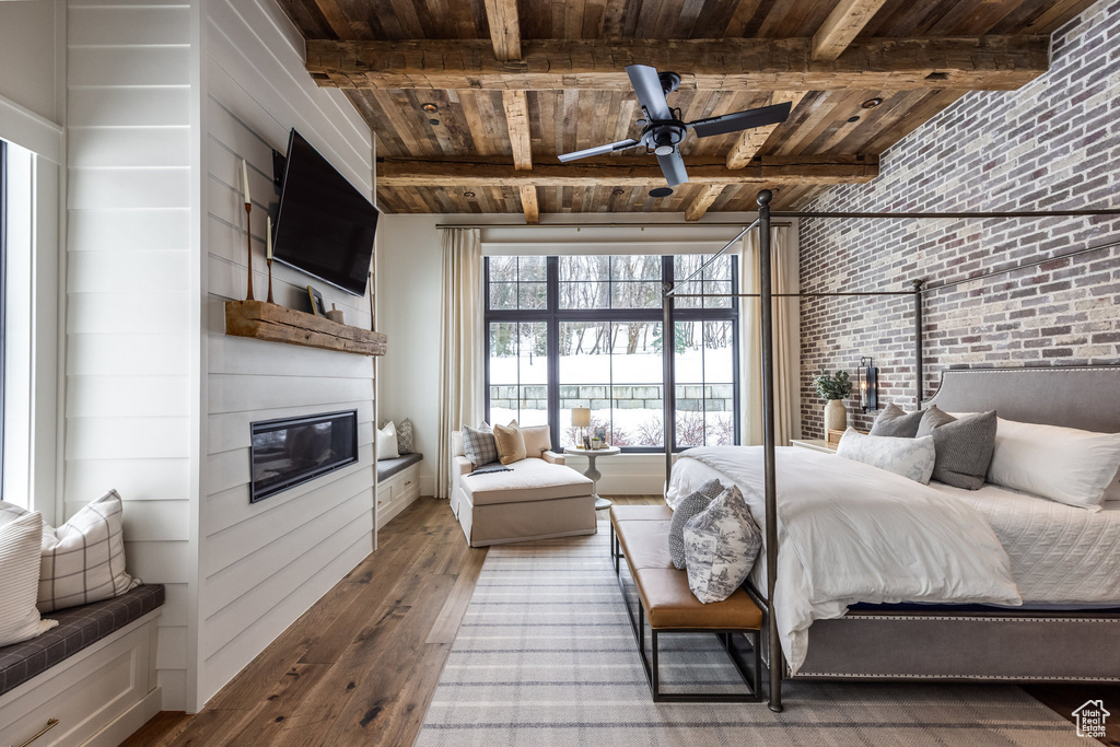 Bedroom featuring wood-type flooring, wood ceiling with exposed beams, a large fireplace, and brick wall