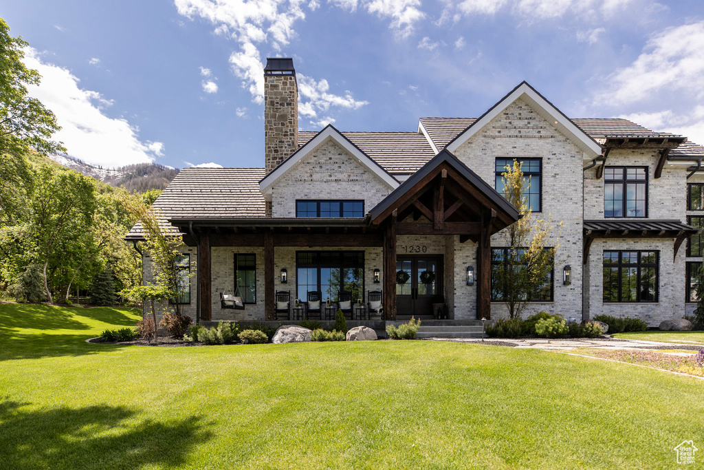 View of front of home with a front lawn, brick siding, a chimney, a porch, and a tile roof