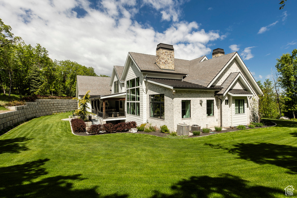 Back of house with a sunroom, a chimney, a yard, and central air condition unit