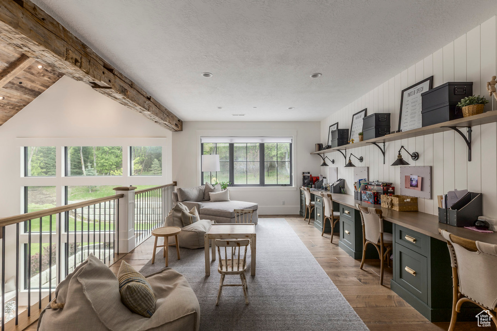 Living area featuring light wood finished floors, beam ceiling, an office area, a textured ceiling, and baseboards