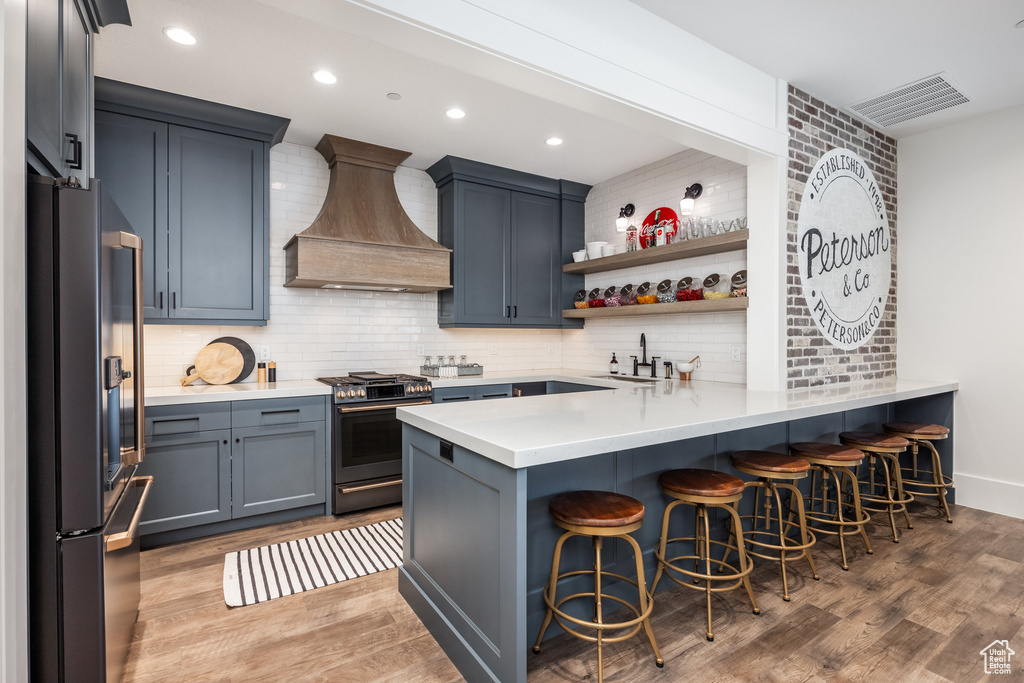 Kitchen featuring refrigerator, gas range, custom exhaust hood, a peninsula, and a sink