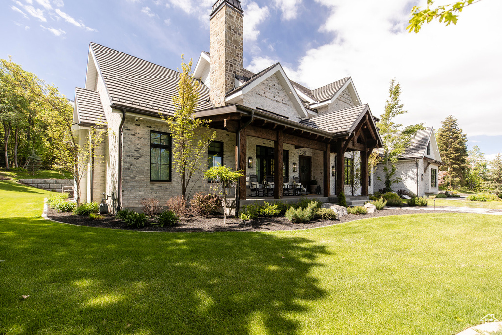 Back of house featuring brick siding, a yard, a chimney, and covered porch