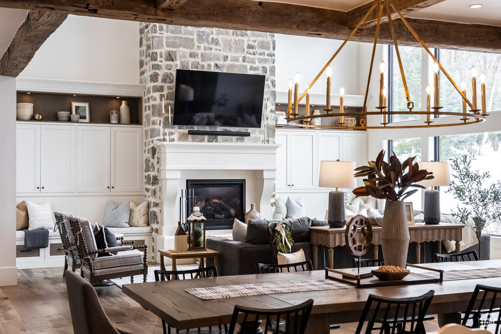 Dining space with wood finished floors, a chandelier, a glass covered fireplace, beamed ceiling, and a towering ceiling