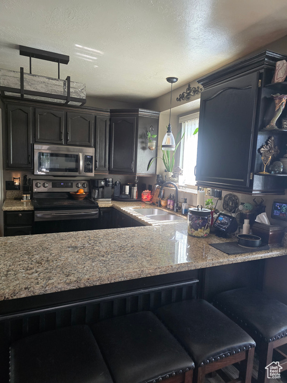 Kitchen with a sink, decorative light fixtures, stainless steel appliances, a peninsula, and light stone countertops