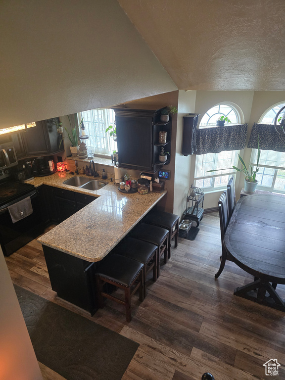 Kitchen with a sink, a kitchen breakfast bar, a textured ceiling, dark wood-style floors, and a peninsula
