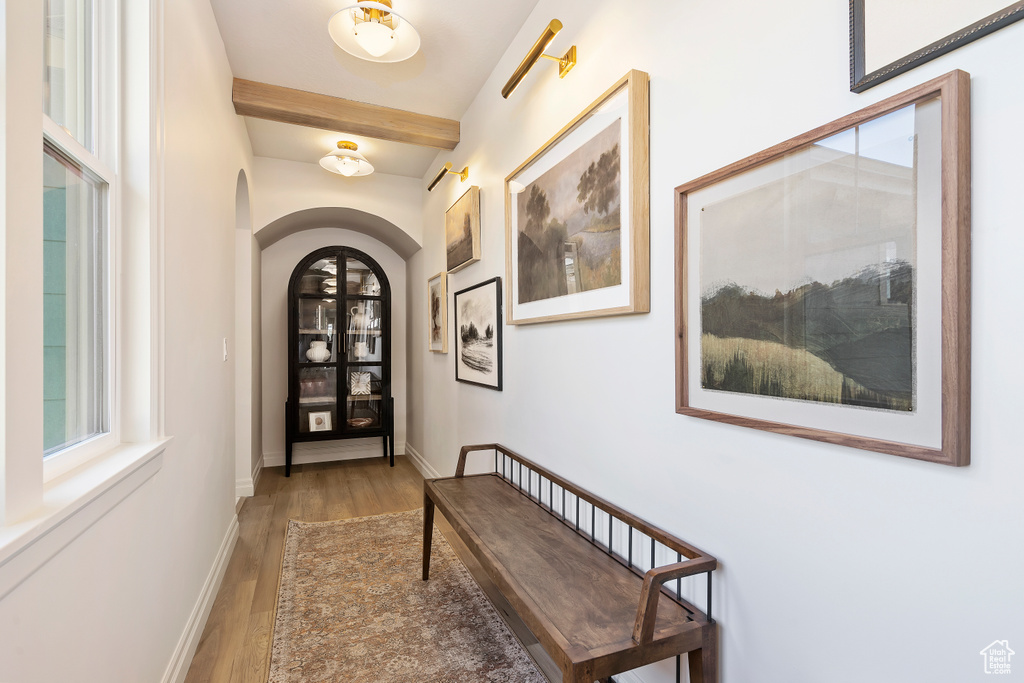 Doorway with arched walkways, beamed ceiling, baseboards, and wood finished floors
