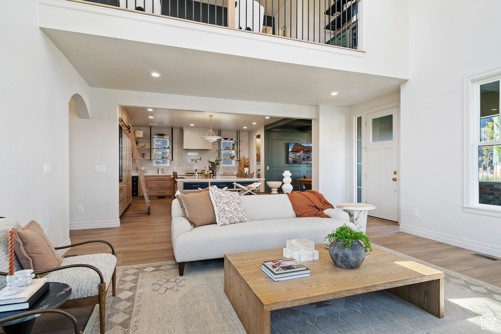Living room featuring light wood-style floors, arched walkways, visible vents, and a high ceiling