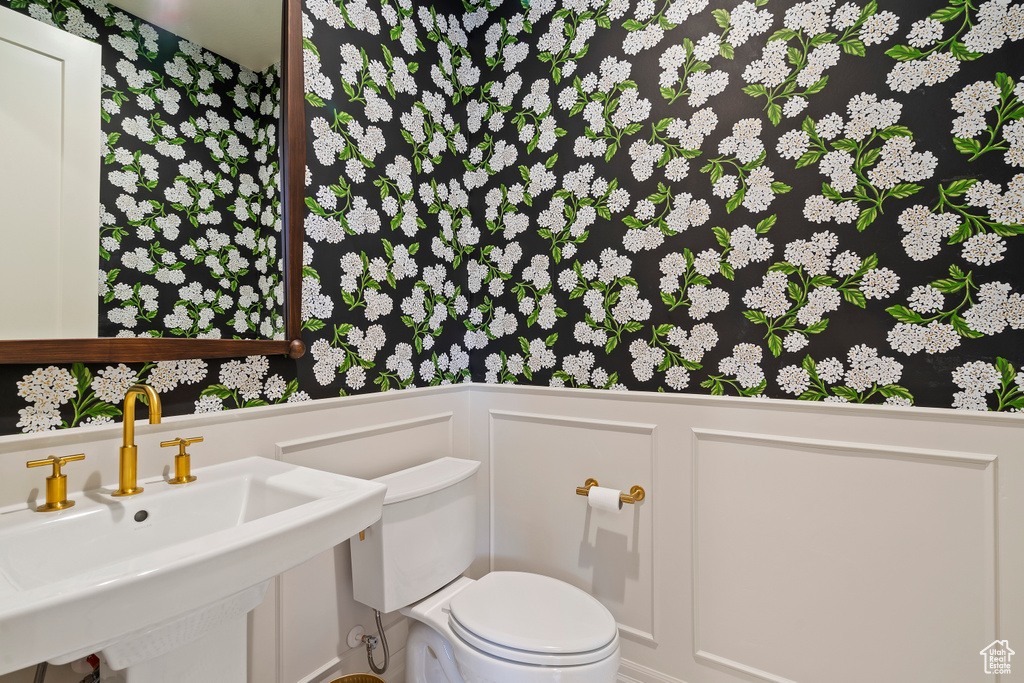 Bathroom featuring a wainscoted wall, a sink, toilet, and a decorative wall