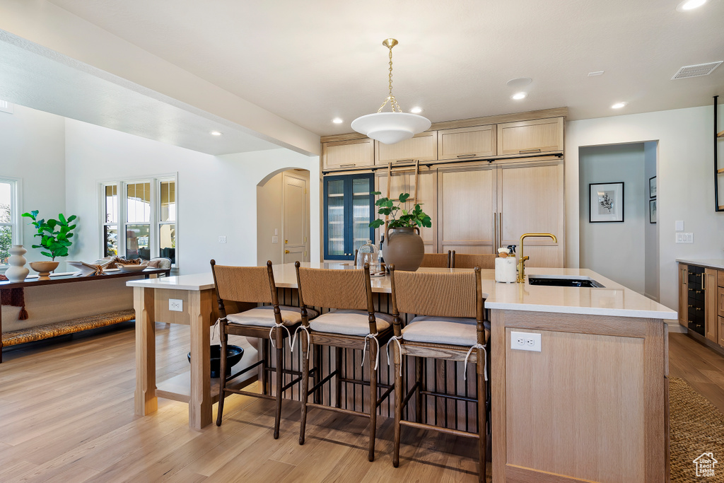 Kitchen with arched walkways, visible vents, light wood-style flooring, a kitchen island with sink, and a sink