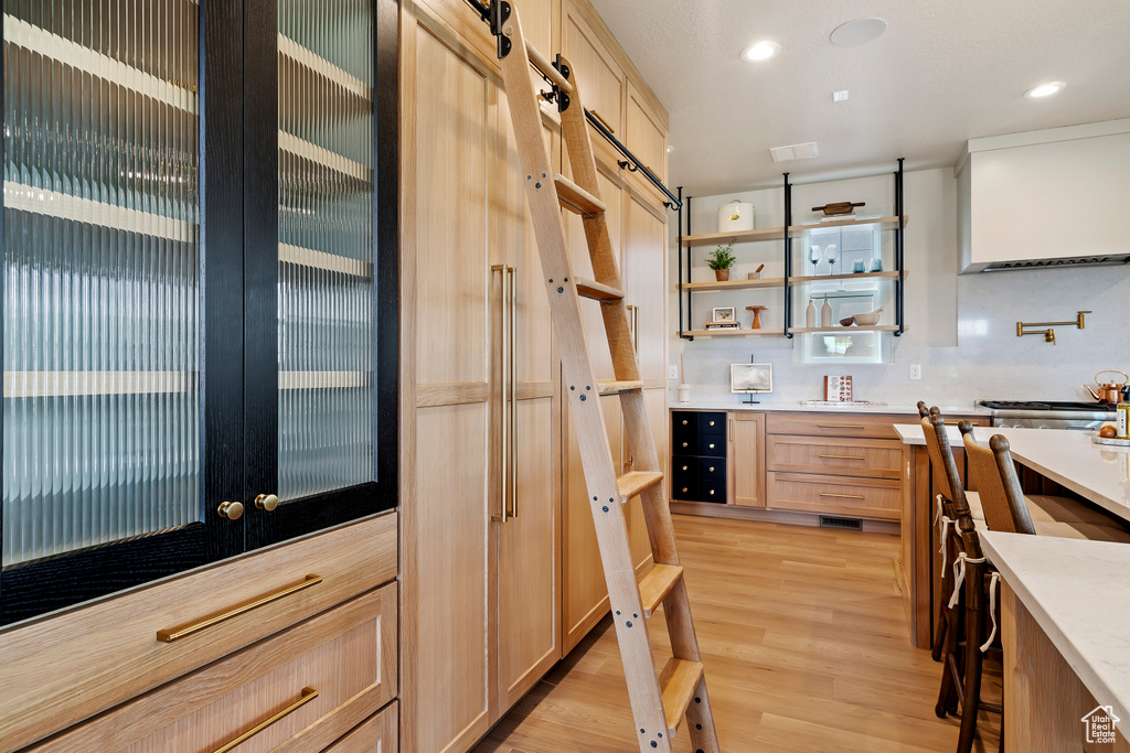 Kitchen with light wood finished floors, recessed lighting, light countertops, glass insert cabinets, and light brown cabinets