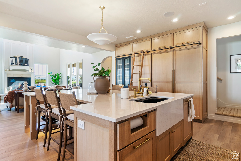 Kitchen featuring a center island with sink, arched walkways, open floor plan, light wood-style floors, and a sink