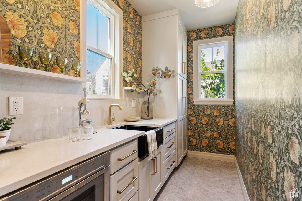 Kitchen with a sink, baseboards, white cabinets, light countertops, and wallpapered walls