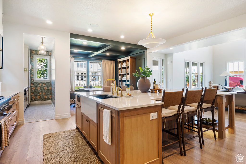 Kitchen featuring coffered ceiling, a sink, open floor plan, a large island, and light wood finished floors