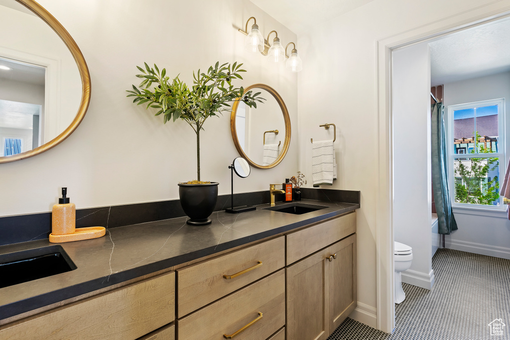 Full bathroom featuring a bathing tub, toilet, a sink, baseboards, and double vanity