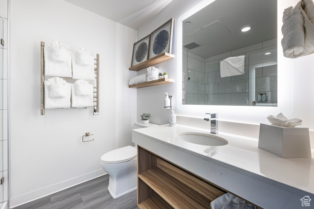 Full bath featuring vanity, wood finished floors, toilet, a tile shower, and baseboards