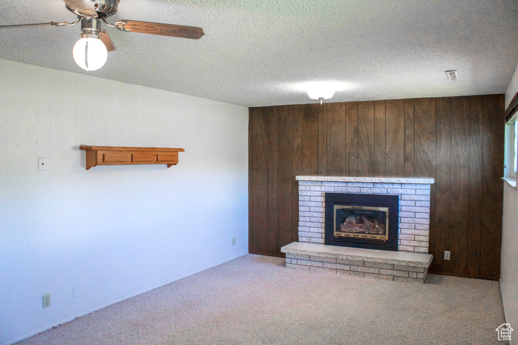Unfurnished living room with a fireplace, wood walls, carpet, and a textured ceiling