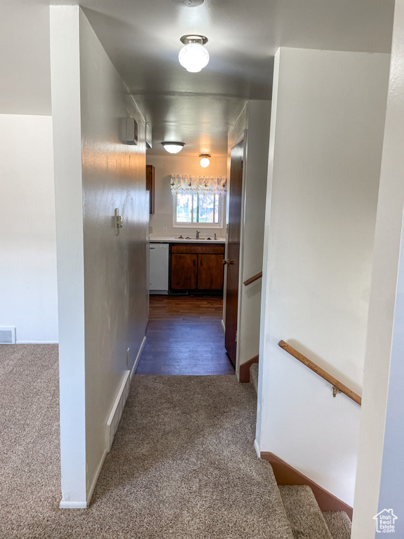 Corridor featuring a sink, baseboards, dark colored carpet, and visible vents