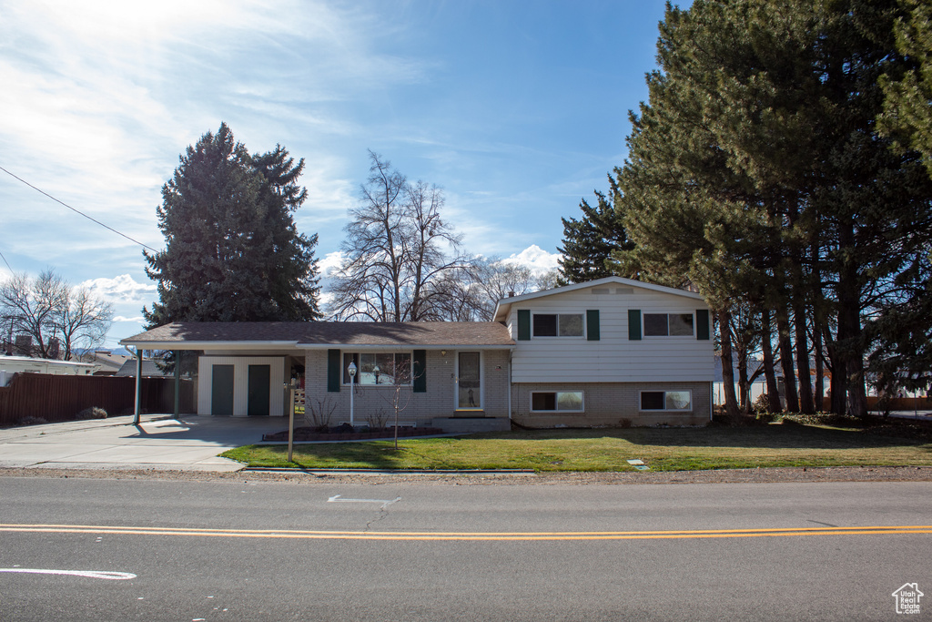 Split level home featuring fence, an attached carport, brick siding, a front lawn, and driveway