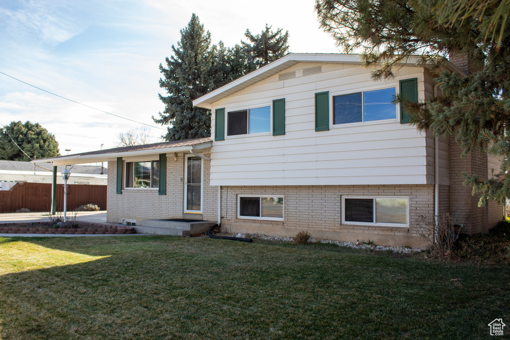 Tri-level home featuring an attached carport, a front yard, fence, and brick siding