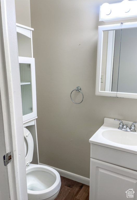 Bathroom featuring toilet, vanity, baseboards, and wood finished floors