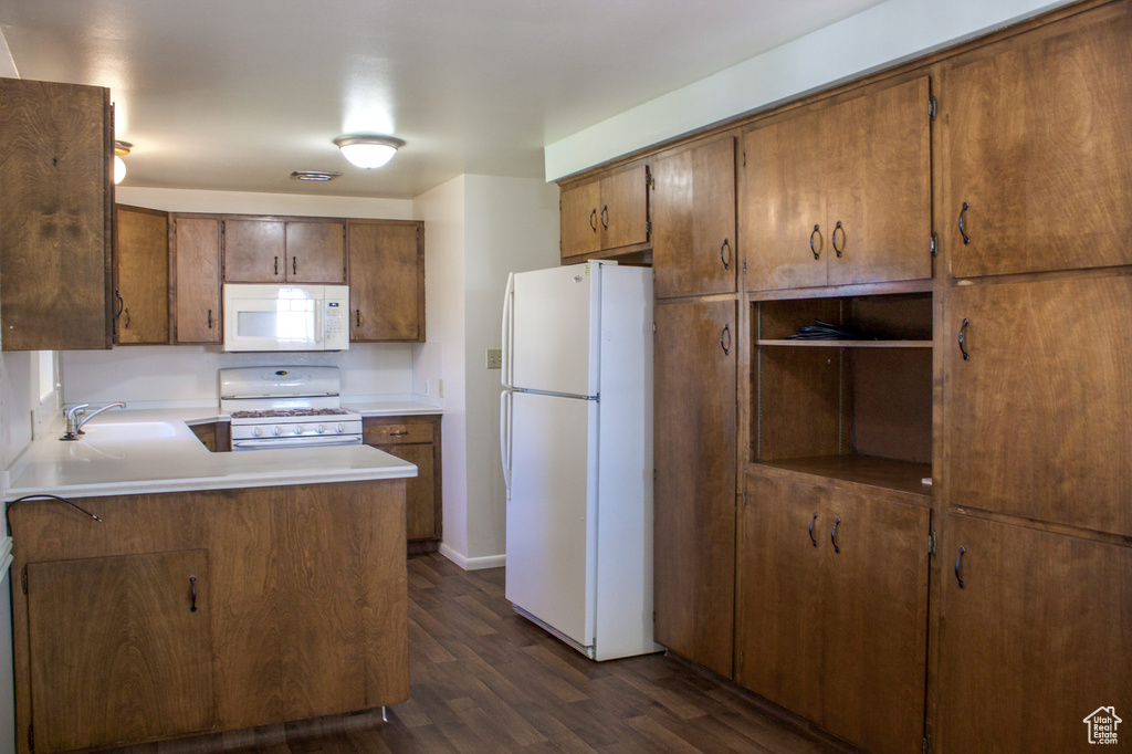 Kitchen with light countertops, a peninsula, white appliances, dark wood-type flooring, and a sink