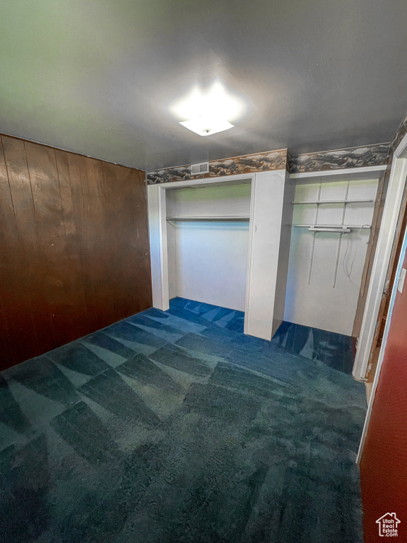 Unfurnished bedroom with wood walls and dark carpet