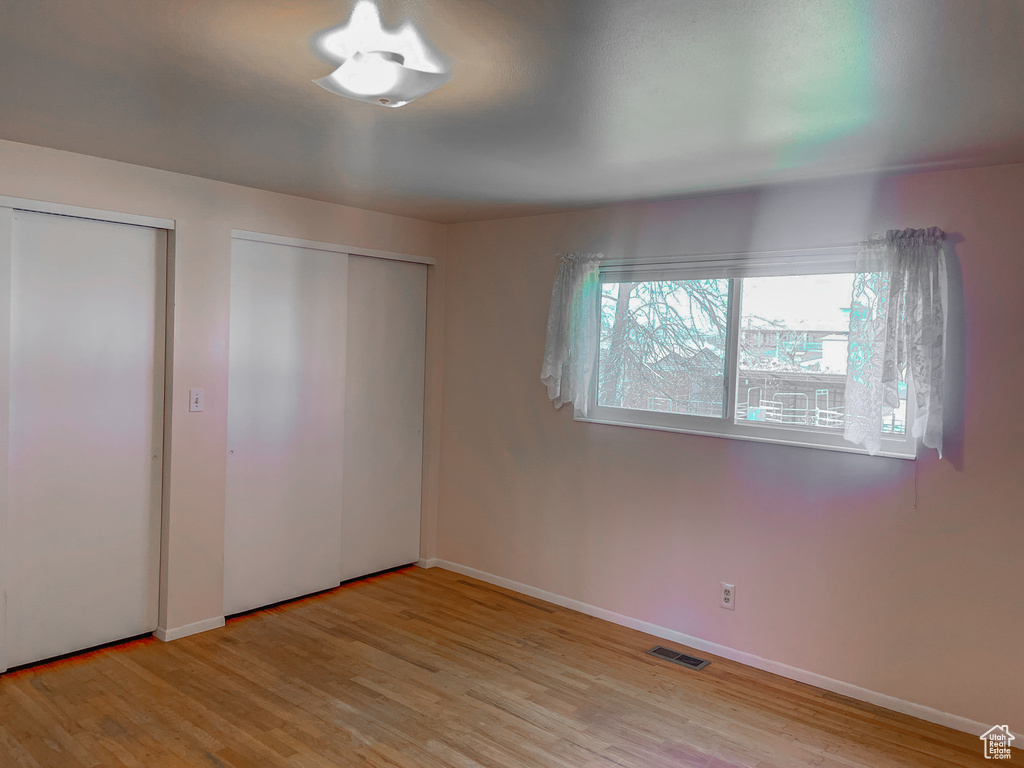Unfurnished bedroom with baseboards, visible vents, light wood-style floors, and two closets