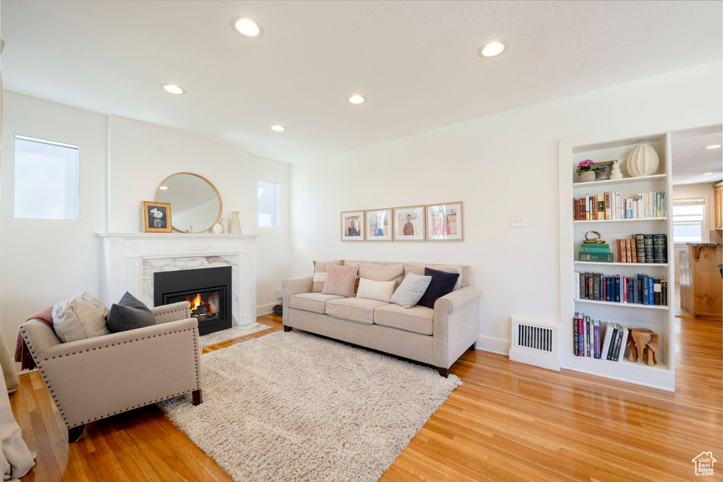 Living room with recessed lighting, light wood-style floors, visible vents, a high end fireplace, and built in features