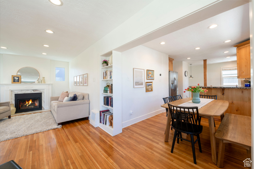 Dining room with baseboards, recessed lighting, a high end fireplace, and light wood-style floors