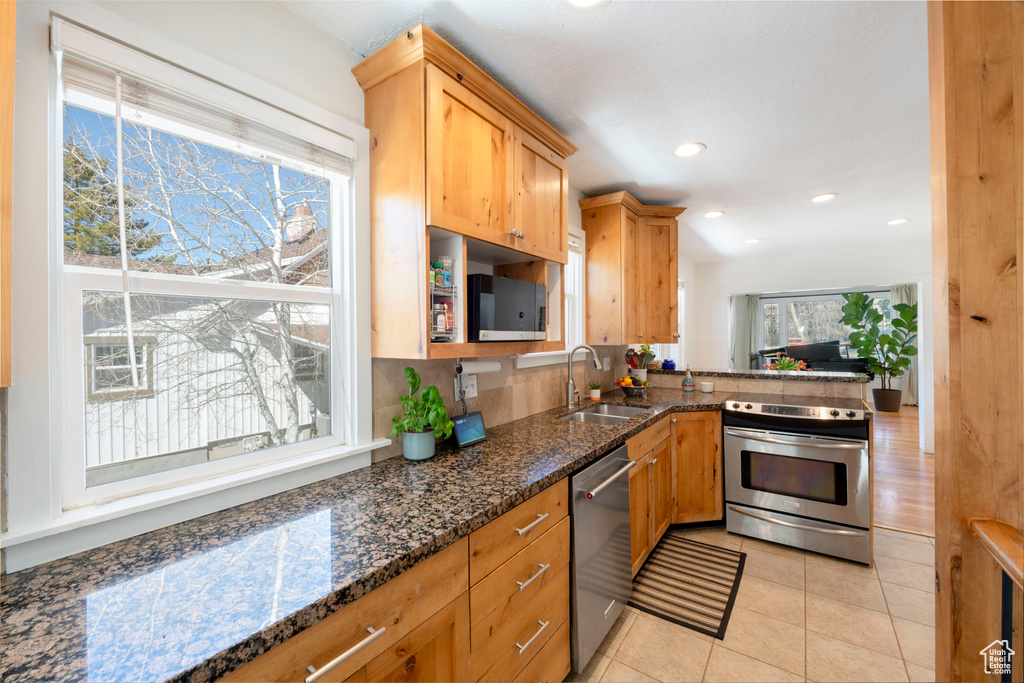 Kitchen featuring recessed lighting, light tile patterned floors, stainless steel appliances, dark stone counters, and a sink