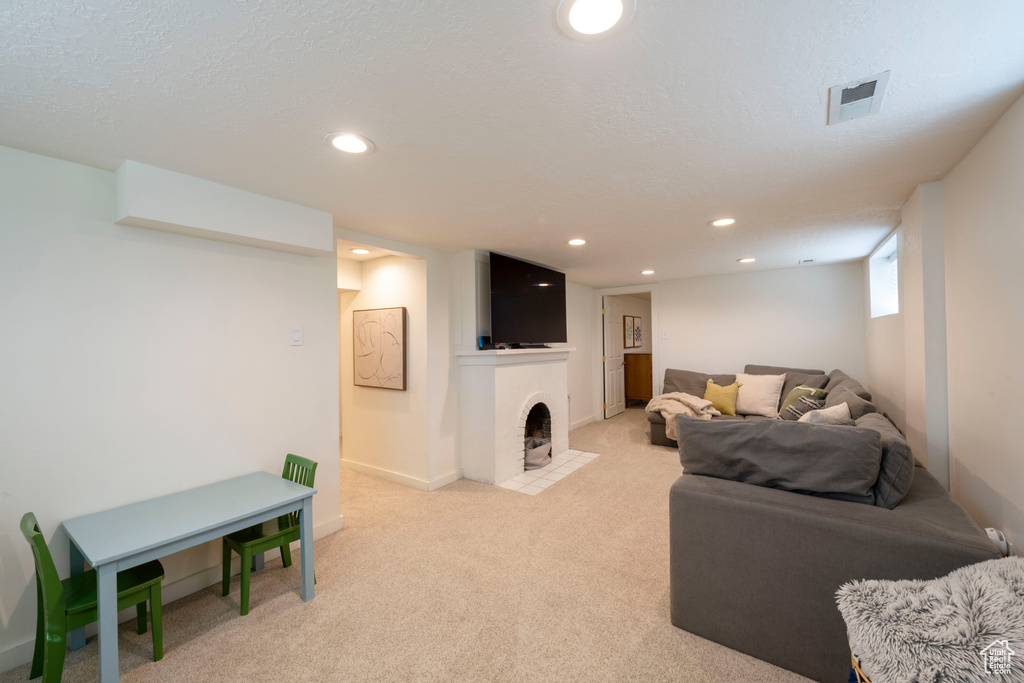 Living area with a fireplace with flush hearth, light colored carpet, visible vents, and recessed lighting