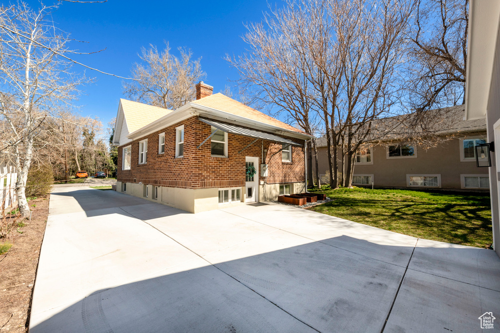 Rear view of property featuring a chimney, concrete driveway, brick siding, a yard, and a patio area