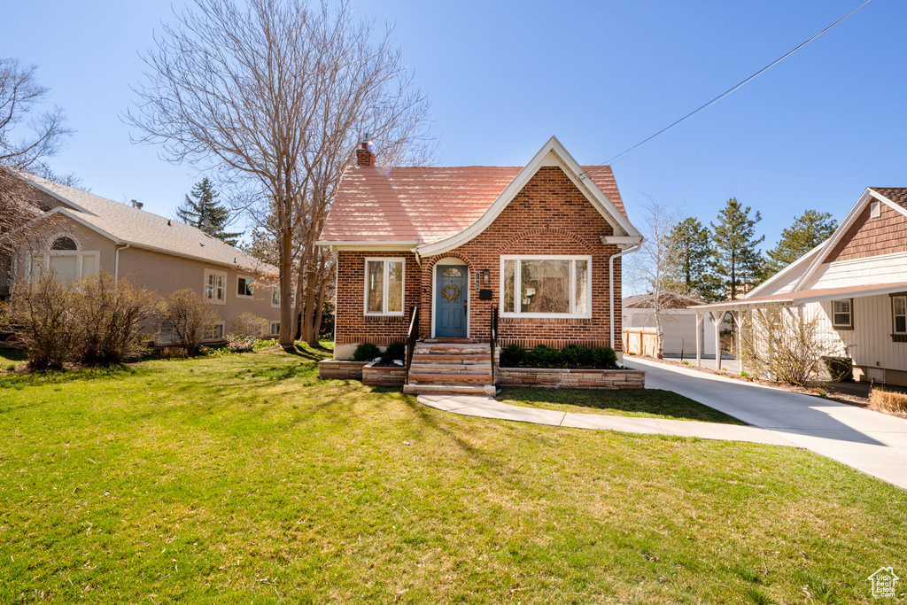 View of front of house with driveway, brick siding, a chimney, and a front yard