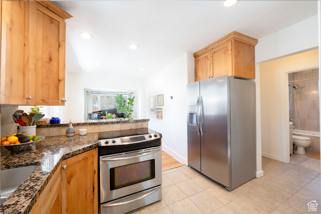 Kitchen featuring appliances with stainless steel finishes, a peninsula, dark stone countertops, light tile patterned floors, and recessed lighting