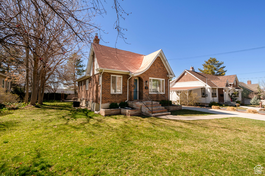 View of front facade with a chimney, a front yard, brick siding, and driveway