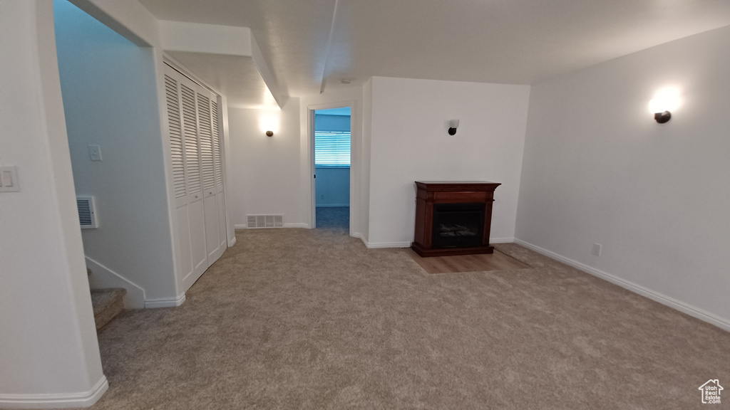 Unfurnished living room featuring carpet flooring, a fireplace with flush hearth, and baseboards