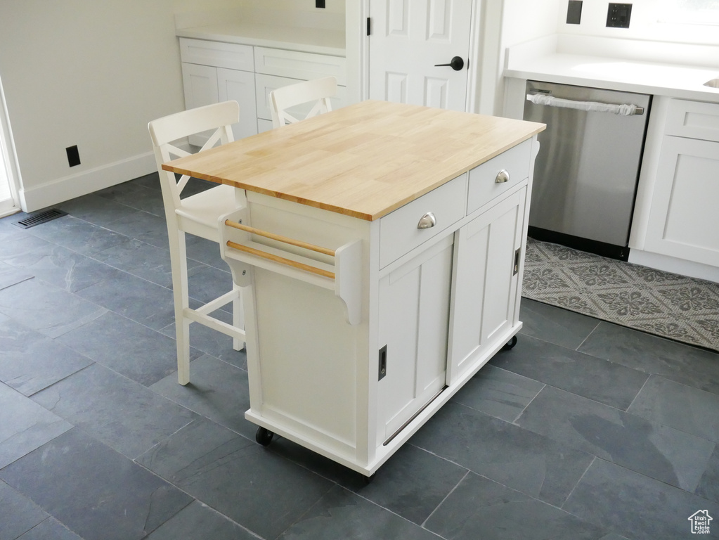 Kitchen with dishwasher, white cabinetry, butcher block countertops, and a kitchen bar