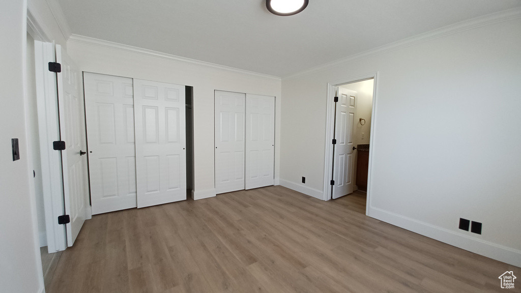 Unfurnished bedroom with multiple closets, light wood finished floors, ornamental molding, baseboards, and ensuite bathroom