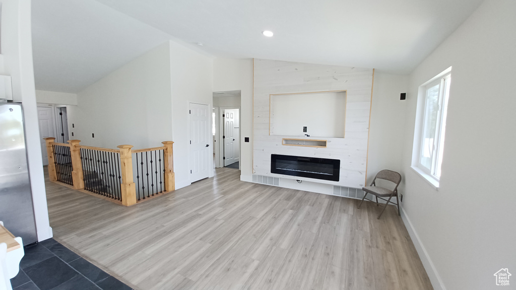 Unfurnished living room featuring lofted ceiling, wood finished floors, baseboards, a fireplace, and recessed lighting