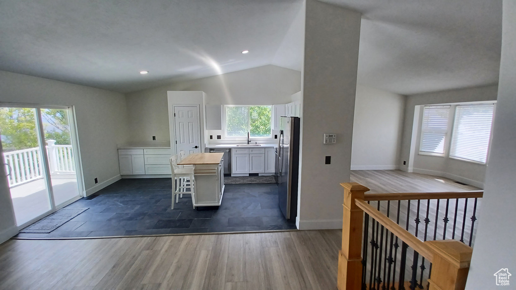 Kitchen with vaulted ceiling, a sink, white cabinets, a kitchen island, and baseboards