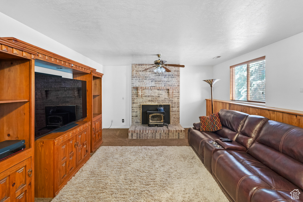 Carpeted living area featuring a wood stove, a ceiling fan, and a textured ceiling