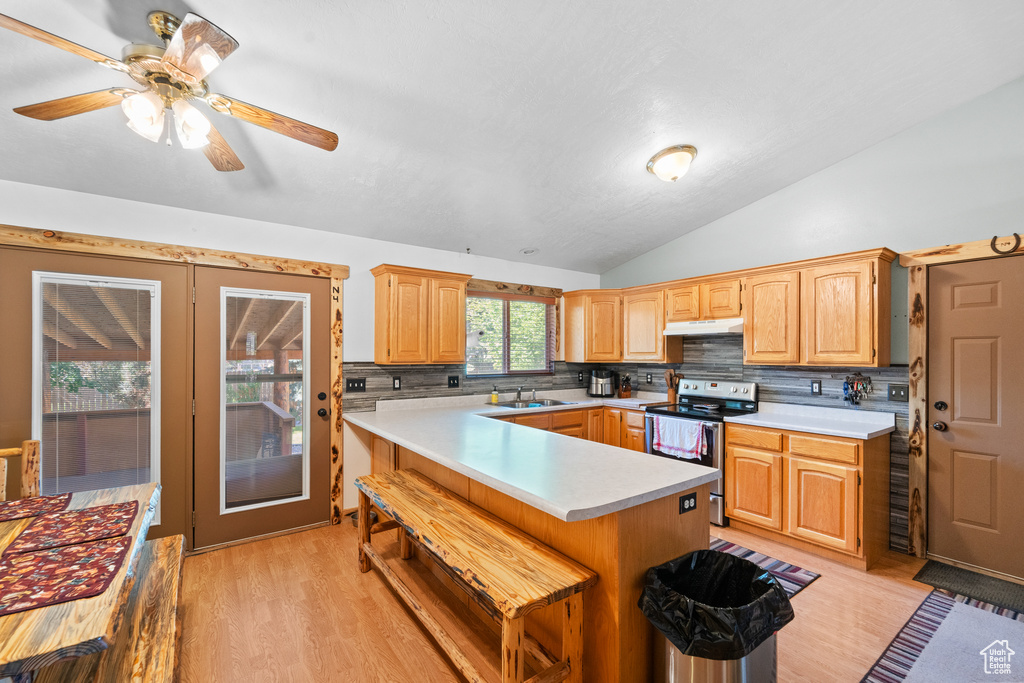 Kitchen featuring stainless steel range with electric stovetop, light countertops, under cabinet range hood, light wood-style floors, and lofted ceiling