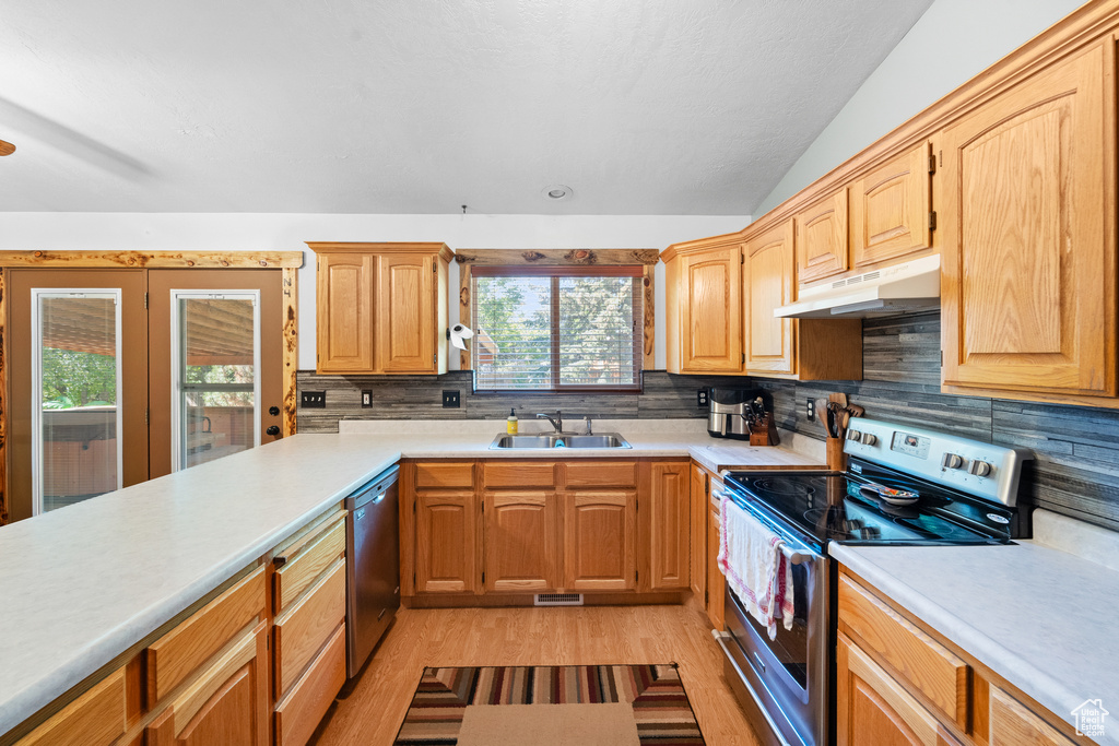 Kitchen featuring appliances with stainless steel finishes, under cabinet range hood, a sink, light wood-type flooring, and light countertops