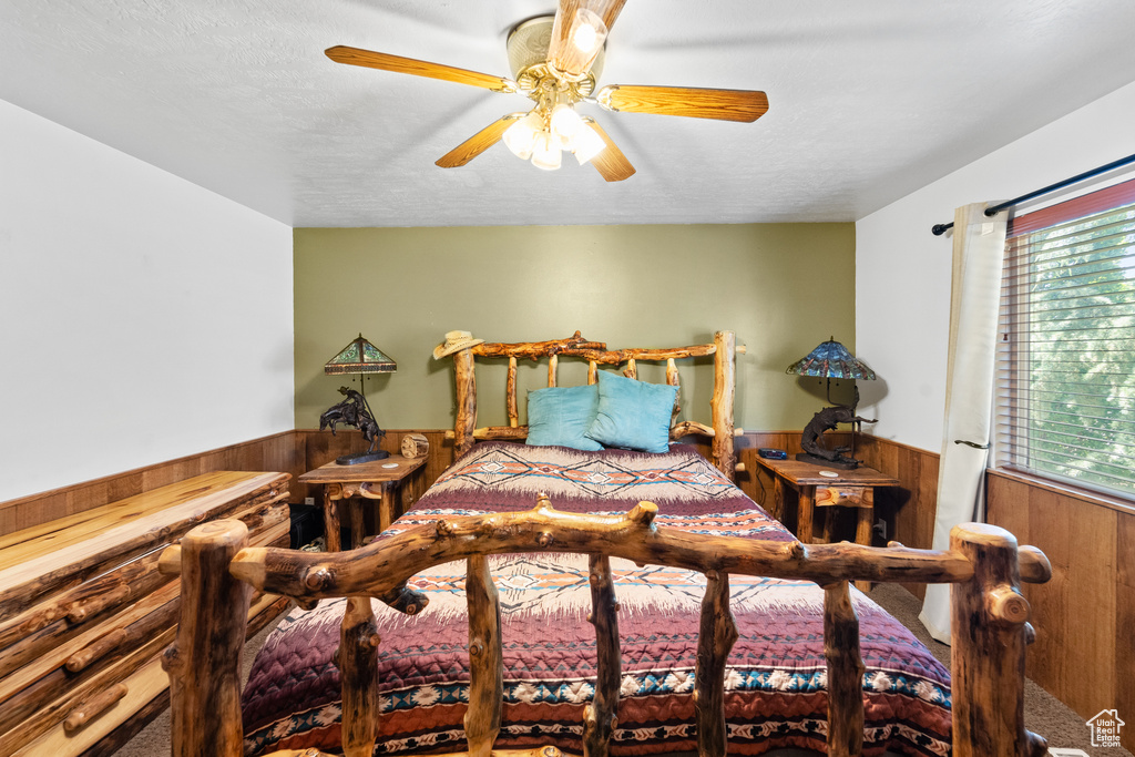 Bedroom featuring wainscoting, wooden walls, carpet flooring, ceiling fan, and a textured ceiling